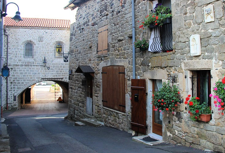 Colourful flowers decorate a house and an arch covers the road leading out of Pradelles