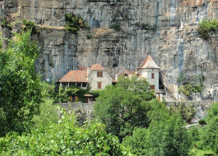 Stone cliff face with houses directly in front, shrubs and greenery in the foreground, Cabrerets