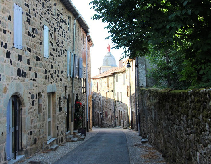 Stone houses flank a narrow lane. The domed roof of Chapelle Notre-Dame, crowned by a statue of the Virgin Mary, is visible above the rooftops