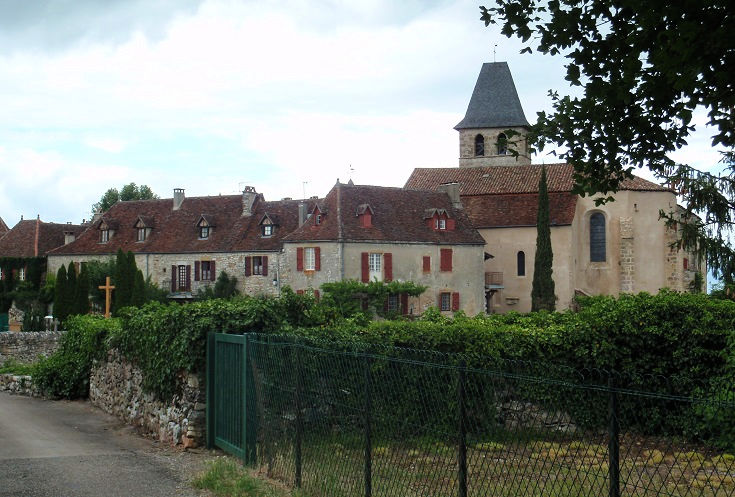 Pale stone walls and deep red roof tiles of the long, low façade of the château in Loubressac