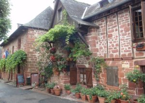 Dark red stone buildings with wisteria vines and colourful pot plants