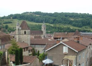 Rooftops of the houses and church in Figeac set to the fore of green fields and a treed ridge