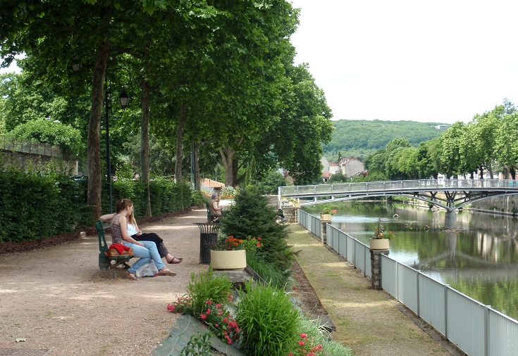 Two girls relax on park benches near the river in Figeac
