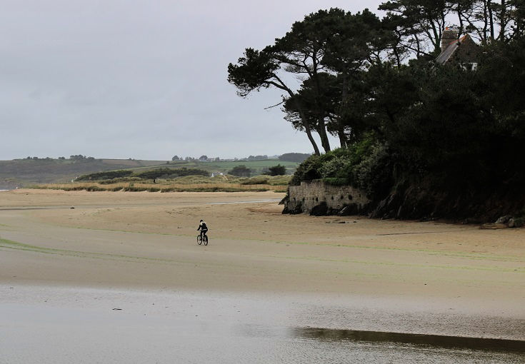 A cyclist rides along the sand on Plage de Sainte-Anne, Brittany
